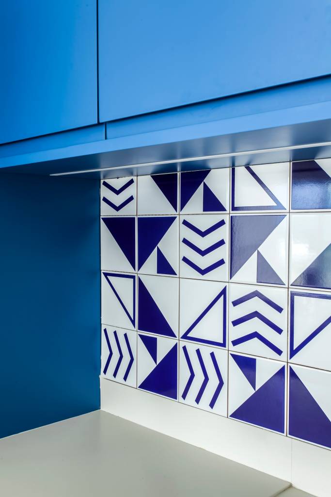 Apê tem décor inspirado na praia com toques azuis e porcelanato areia. Projeto de Korman Arquitetos. Na foto, marcenaria de cozinha, backsplash de azulejos geométricos.