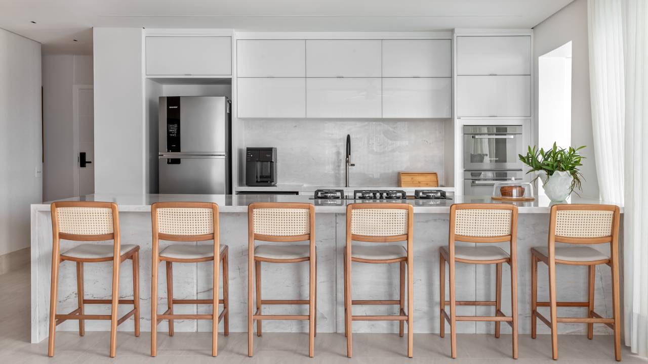 À beira-mar, apartamento de 160 m² traz uma estética clean e atemporal. Projeto de Mezzure Arquitetura. Na foto, cozinha americana como bancada. bancos e cortinas.
