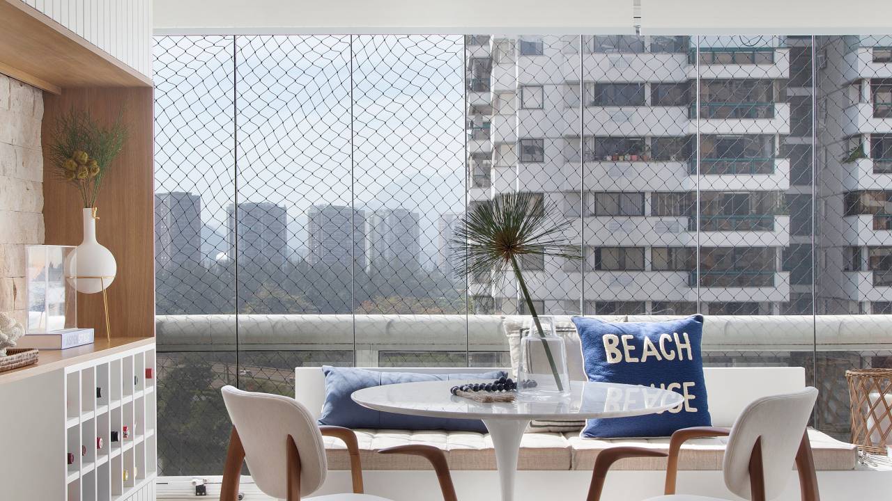 Canto alemão na varanda cria local perfeito para café da manhã em apê. Projeto de Memoá Arquitetos. Na foto, varanda integrada com mesa branca redonda, nicho com bar.