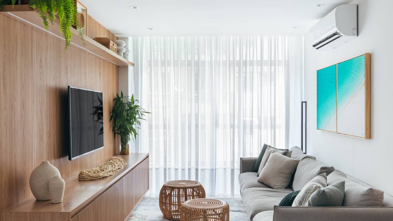 Dois apês viram um com cozinha gourmet, jantar e sala de TV integradas. Projeto de Fernanda Medeiros. Na foto, sala, cortina, cestos, sofá cinza, parede com painel de madeira.