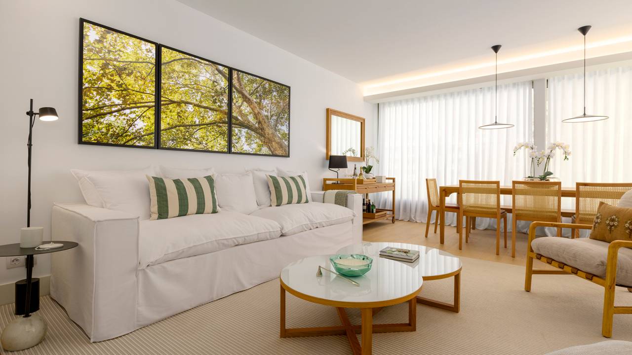 Feito à distância, apê de 160 m² em Portugal ganha décor com clima carioca. Projeto de C.W. Arquitetura. Na foto, sala de estar e jantar com quadros na parede, sofá e mesas.