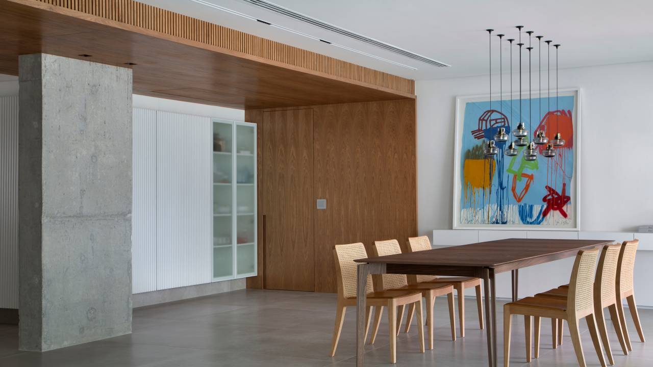 Venezianas em madeira trazem privacidade aos espaços de apê minimalista. Projeto de PKB Arquitetura. Na foto, sala integrada, piso de porcelanato, mesa de jantar, quadro.