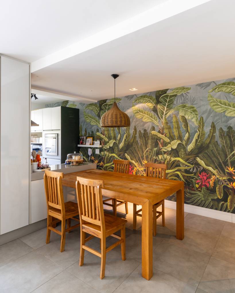 Apartamento em São Paulo tem decoração leve com livros e plantas. Projeto de Sou Arquitetura. Na foto, sala de jantar, mesa e cadeiras de madeira, papel de parede com tema floresta.