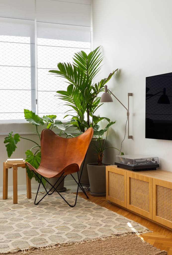 Apê ganha escritório com vista para o mar e texturas nas paredes brancas. Projeto Ateliê Concreto. Na foto, sala com tapete, poltrona, tv e aparador com porta de tela.