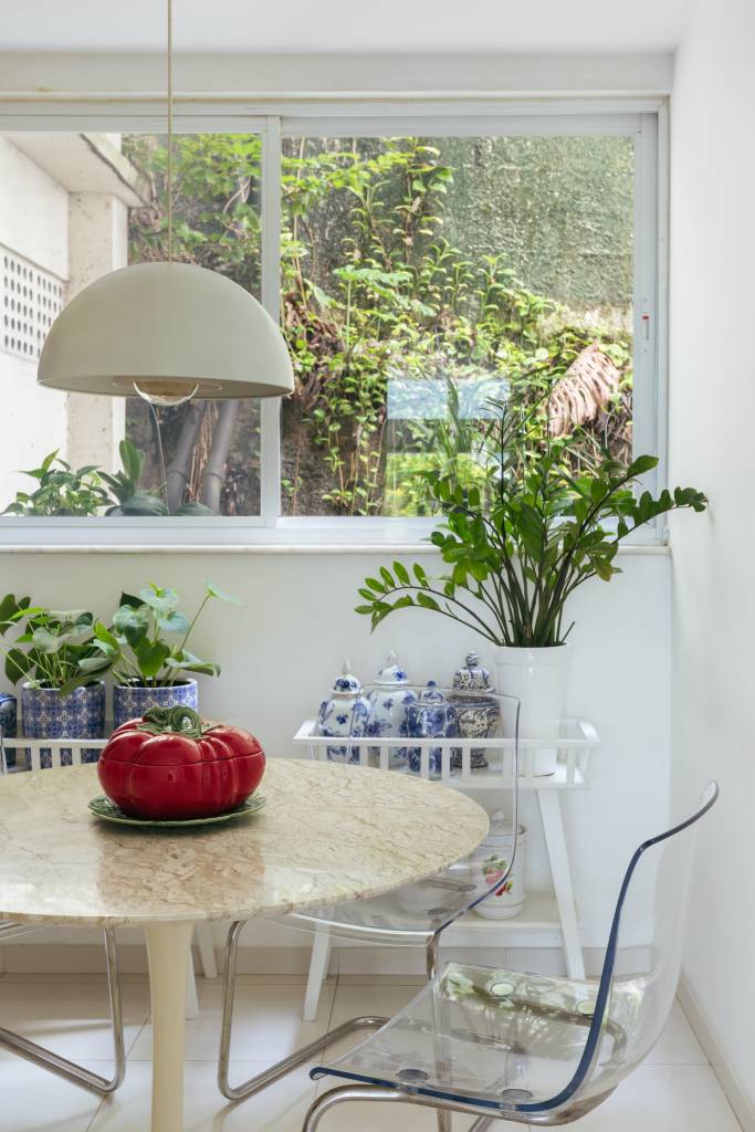 Apê ganha copa de cozinha e suíte voltada para pequeno jardim interno. Projeto de Vivian Reimers. Na foto, mesa redonda pequena, cadeiras transparente, luminária, ar condicionado.