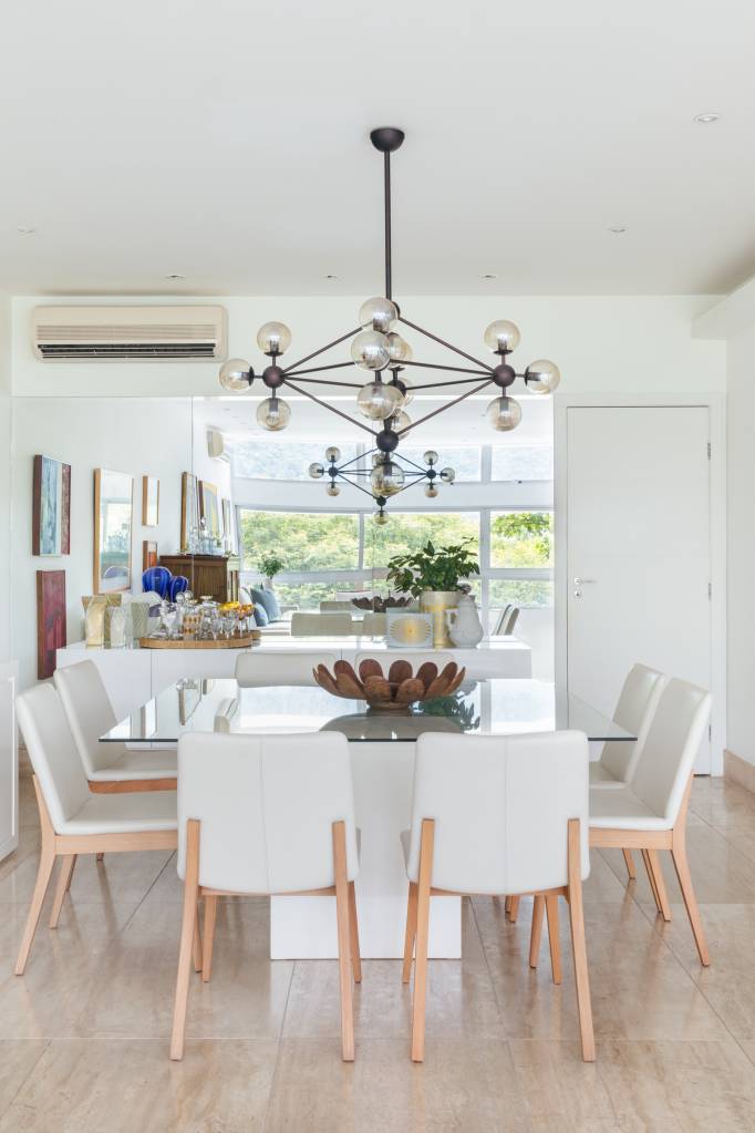 Apê ganha copa de cozinha e suíte voltada para pequeno jardim interno. Projeto de Vivian Reimers. Na foto, sala de jantar, cadeiras brancas, luminária, mesa com tampo de vidro, buffet branco.