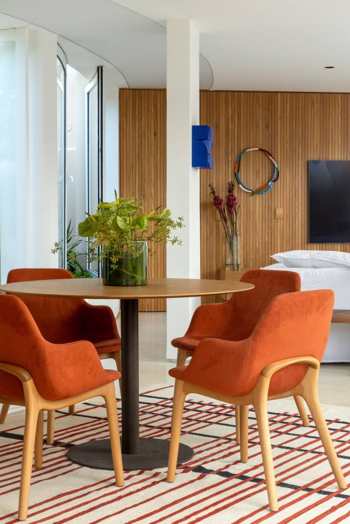 Cobertura com planta circular tem jardim interno, área gourmet e sauna. Projeto de Roberto Souto. Na foto, mesa redonda, tapete, cadeiras laranja.
