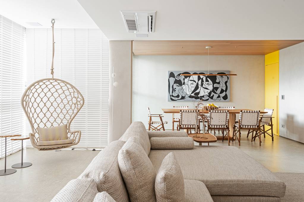 Décor que remete à praia pauta o apê de 140 m² do morador amante do surfe. Projeto do Estúdio Elmor. Na foto, sala de jantar com porta amarela, quadro e cadeira de fita. Varanda com poltrona suspensa.