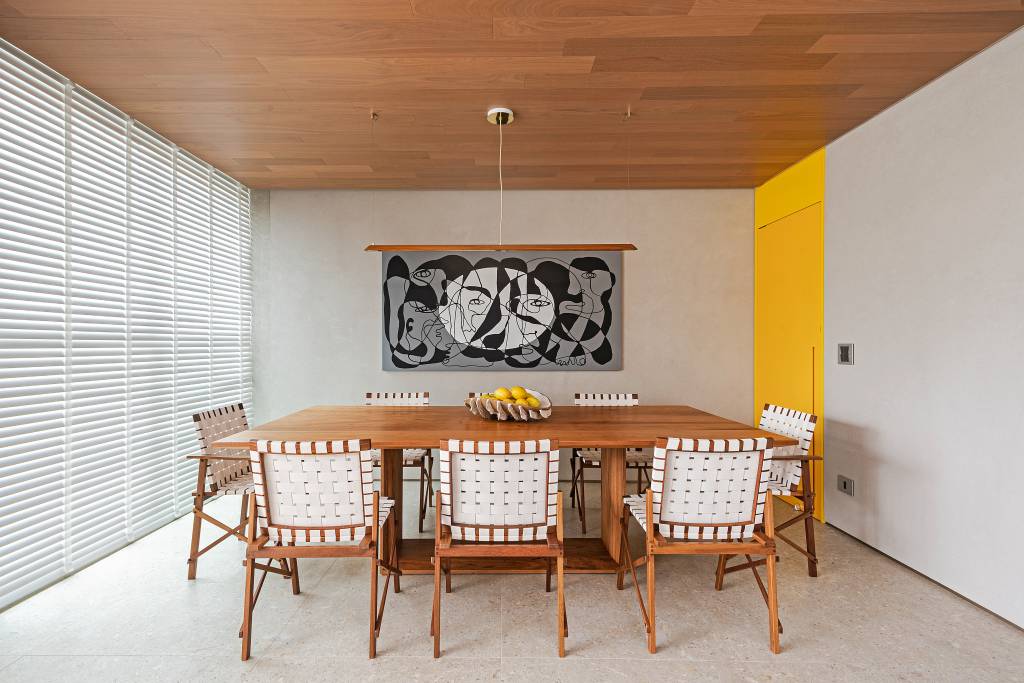 Décor que remete à praia pauta o apê de 140 m² do morador amante do surfe. Projeto do Estúdio Elmor. Na foto, sala de jantar com porta amarela, quadro e cadeira de fita.