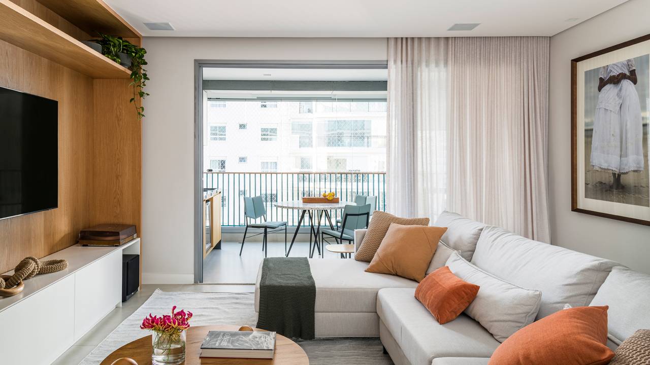 Dois escritórios e ampla área de receber caracterizam apê de 175 m². Projeto de Juliana Casadei. Na foto, sala com tv, painel de madeira, varanda integrada e quadros.