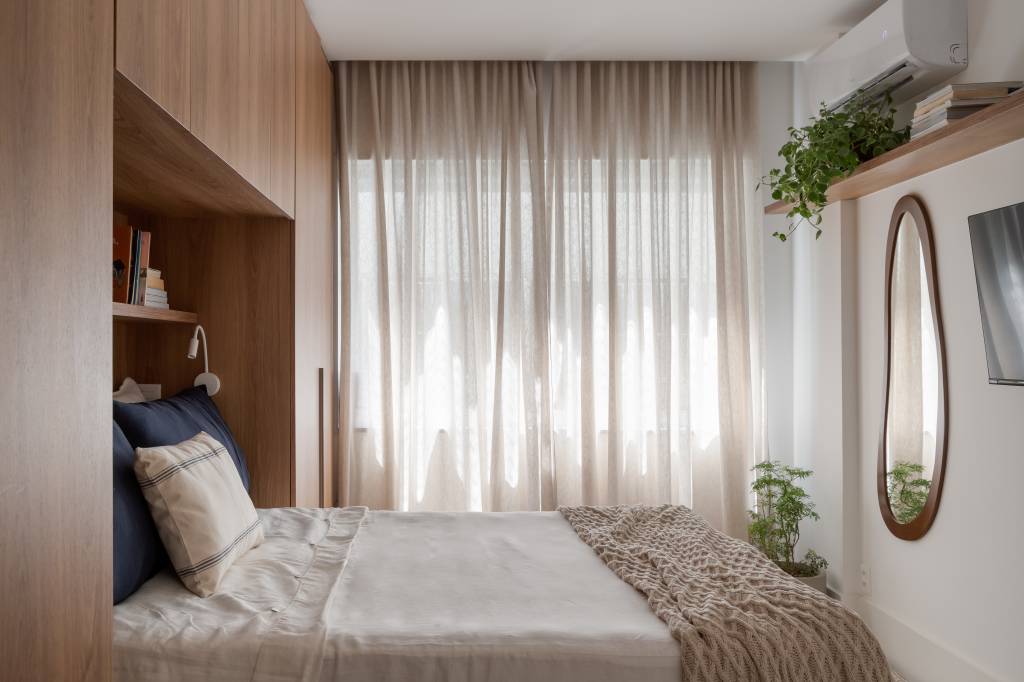 Espelho oval e armário em volta da cama são destaques em apê de 67 m²