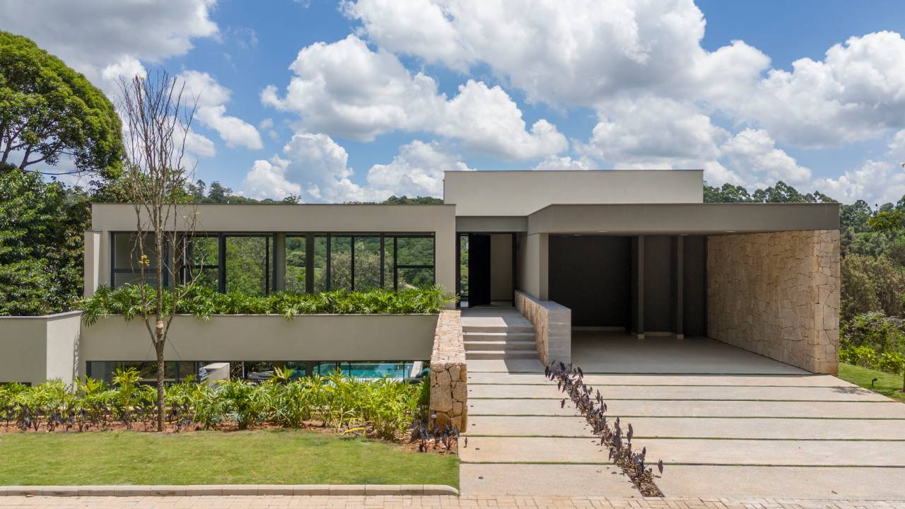 Inspirada no Japão, casa de 524 m² tira proveito da declividade do terreno. Projeto de Cité Arquitetura. Na foto, fachada da casa com jardim e muro de pedra,