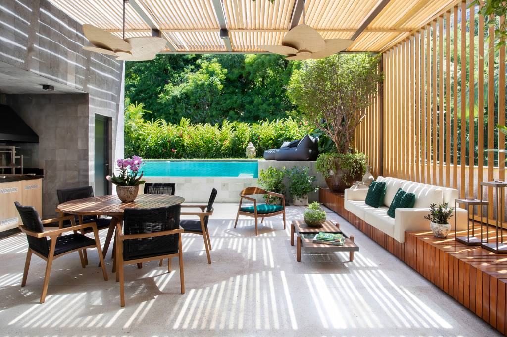 Jardim de apê tem horta com plantas e frutas que atraem aves e borboletas. Paisagismo de Horto Girassol. Na foto, área gourmet externa, mesa de madeira redonda, churrasqueira, piscina.