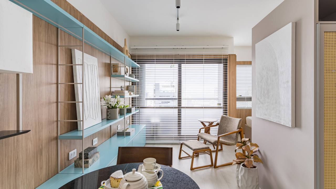 Quarto de hotel vira miniapê com cozinha e estante multifuncional. Projeto de Inovando Arquitetura. Na foto, sala, estante azul, poltrona, mesa redonda pequena.