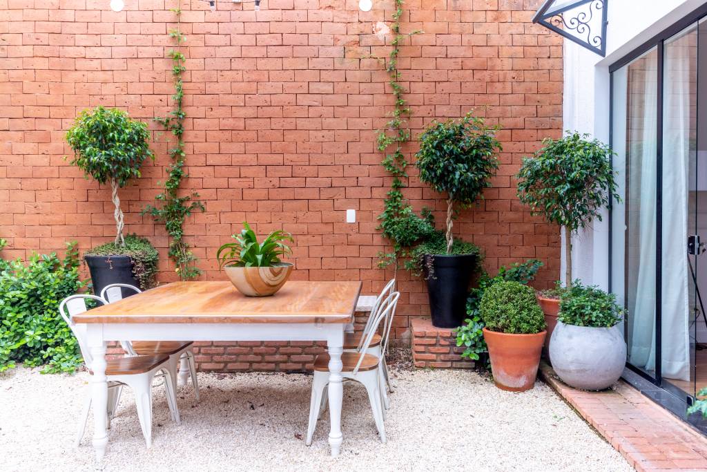 Reforma em casa alugada cria cozinha externa e sala com boiseries. Projeto de Abrazo Interiores. Na foto, área externa com tijolinhos, mesa de madeira.