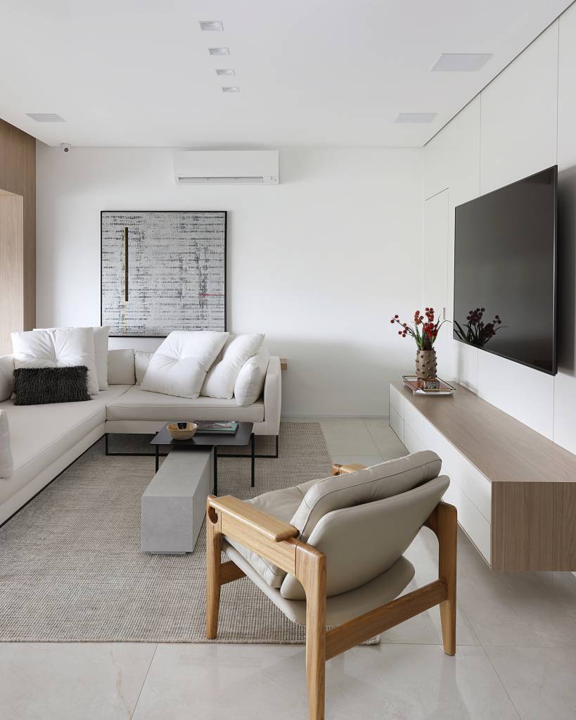 reforma-cria-tres-suites-lindas-area-gourmet-na-varanda-carolina-gava-02-sala Reforma em apê cria três suítes lindas e área gourmet na varanda. Projeto de Carolina Gava. Na foto, sala de estar, sofá branco L, poltrona, rack bege.