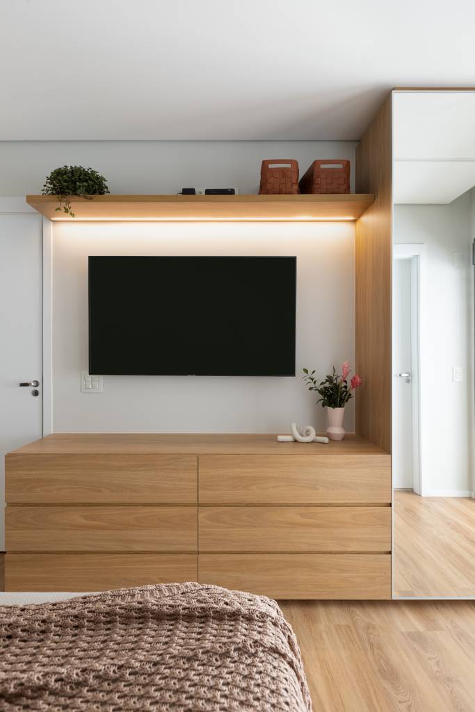 Aconchego e praticidade: apartamento de 126m² possui porcelanato acinzentado neutro e vinílico. Projeto do Estúdio Bena. Na foto, quarto com TV e móvel com gavetas