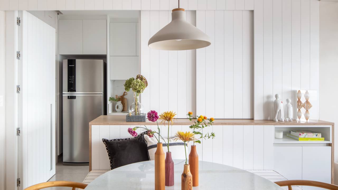 Delicadeza: apê de 66 m² tem cozinha aberta e cabeceira com bordados. Projeto de Memoá Arquitetos. Na foto, cozinha branca com porta de correr de lambri.