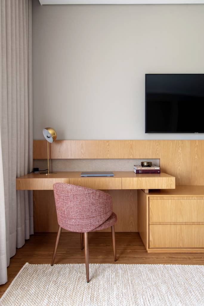 Home office no quarto: arquitetas dão dicas de como compor o ambiente. Projeto de Paiva e Passarini. Na foto, bancada de madeira, cadeira rosa estofada.