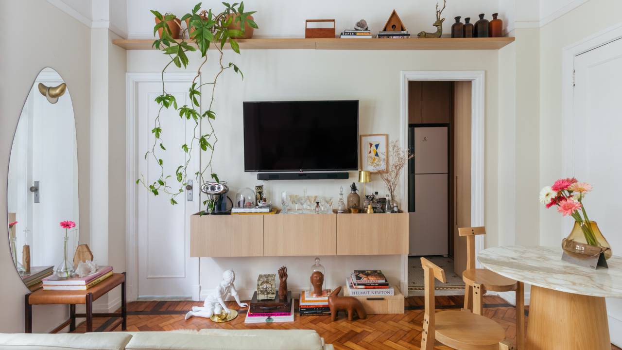Apê de 42 m² em tons de branco e bege tem sala e quarto integrados. Projeto de Rodolfo Consoli. Na foto, sala de estar, sofá, aparador aéreo, prateleira com planta.