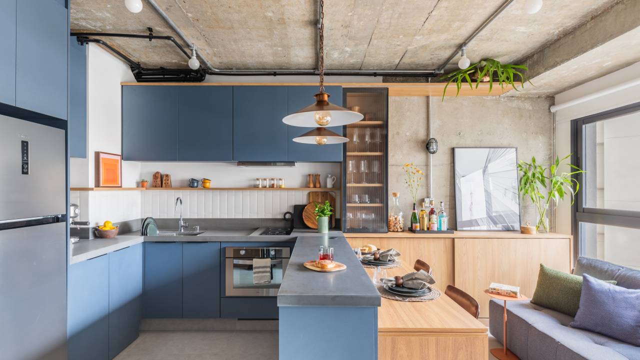 Apê industrial e estiloso de 37 m² tem local armazenamento na cabeceira. Projeto de Studio Guadix. Na foto, cozinha, marcenaria azul, bancada, aparador, cristaleira.