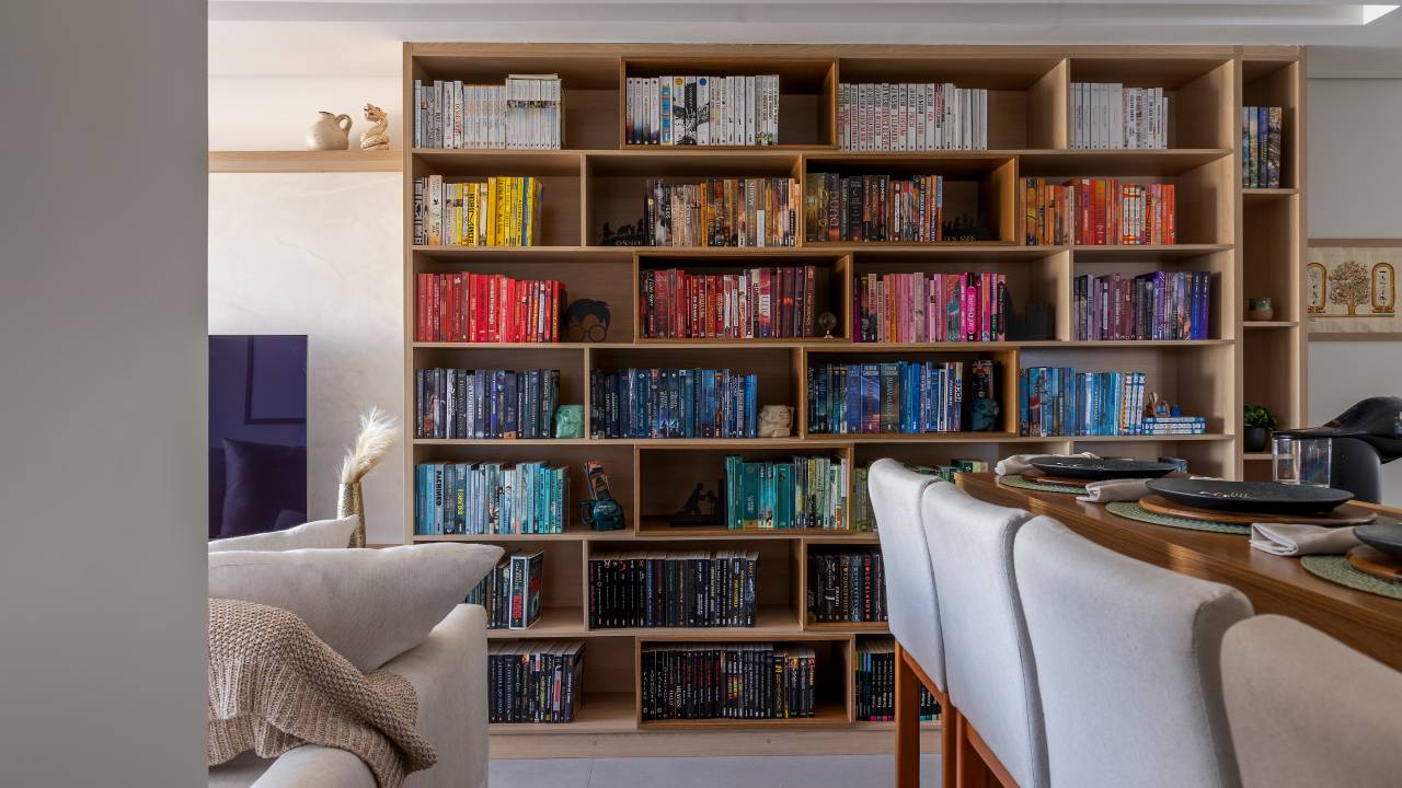 Funkos e livros ganham destaque em reforma de apê de 64 m². Projeto de Vitoria Lacerda. Na foto, sala, estante de livros organizada por cor.