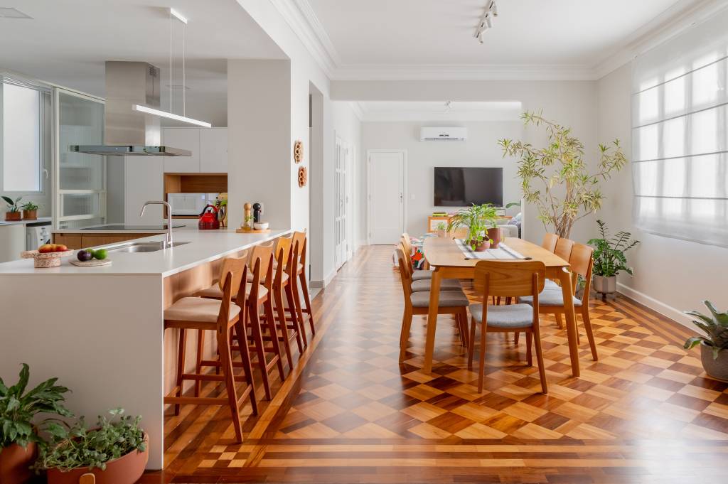 Piso de taco, janelas brancas e sancas dão charme parisiense a este apê. Projeto de Ana Paula Crivelenti. Na foto, sala de estar integrada com cozinha, mesa grande de madeira.