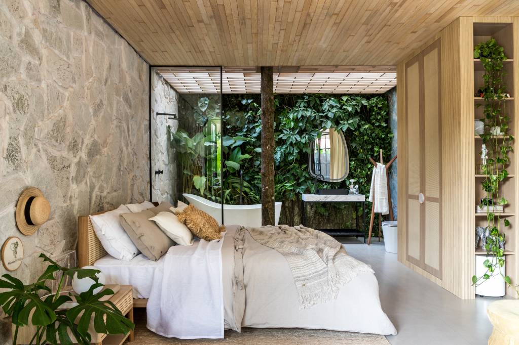 tiny-houses-discutem-sustentabilidade-relacao-com-natureza-casacor-pr-crippa-e-assis-arquitetura-04 3 tiny houses lindas que discutem sustentabilidade e a relação com a natureza. Projeto de Crippa e Assis para a CASACOR PR 2024. Na foto, suíte, parede de pedra, banheiro com jardim.