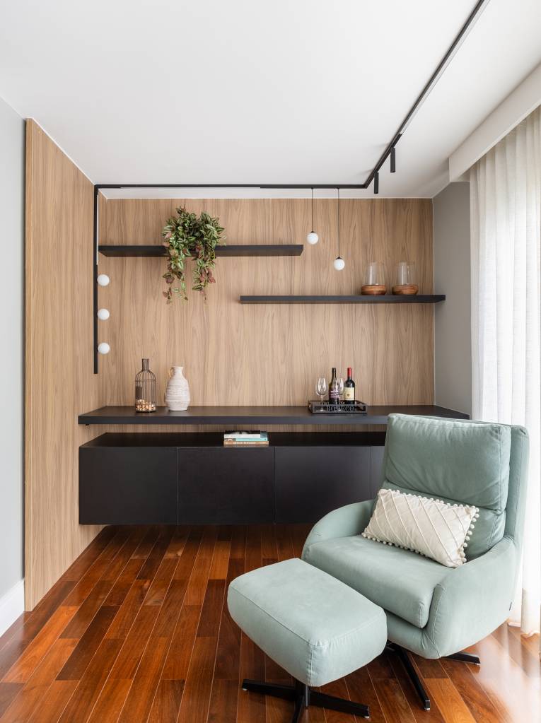 Apê tem cozinha com marcenaria preta e home office com painel ripado branco. Projeto de Duno Arquitetura. Na foto, cantinho de leitura, poltrona com pufe, marcenaria preta.