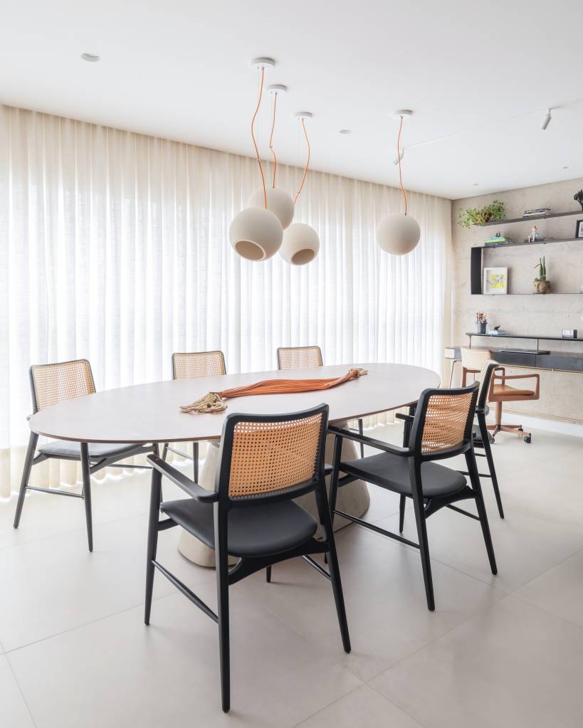 Bancada de lâmina sintetizada integra cozinha e área gourmet neste apartamento. Projeto de BMA Studio. Na foto, sala de jantar, mesa oval, cadeiras com encosto de palhinha.