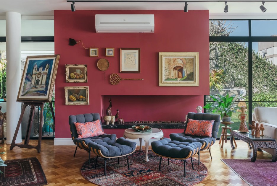 Casa de casal de 70 anos apaixonado por samba inspira-se na brasilidade. Projeto de Ana Cano. Na foto, sala de estar com parede vermelha e poltrona costela com pufe. Piso de taco.