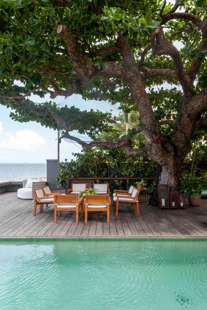 Casa de praia tem estrutura de toras de árvore e pergolados com esteiras em tala de dendê. Projeto de DB Arquitetos. Na foto, piscina, deck, mesa.