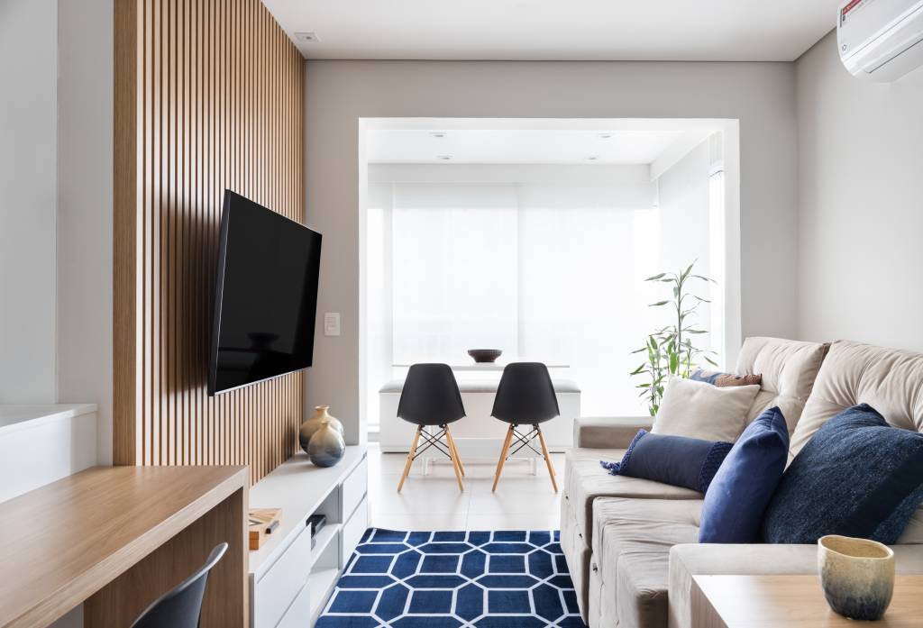 Cozinha com gabinete azul e painel ripado na sala dão textura e cor a apê de 62 m². Projeto de Duno Arquitetura. Na foto, sala de estar integrada com varanda, tapete azul, sofá.