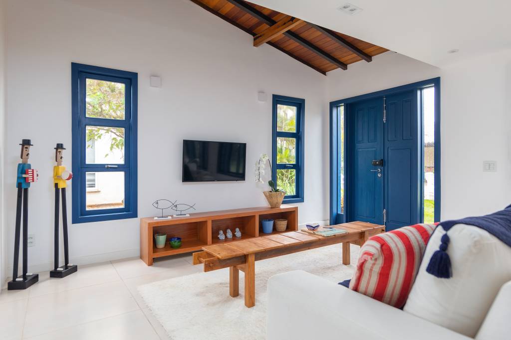 Janelas azuis dão charme a casa de praia em Búzios com suíte térrea escondida por lambris. Projeto de Fernanda Zeitoune. Na foto, sala de estar, mesa de centro de madeira.