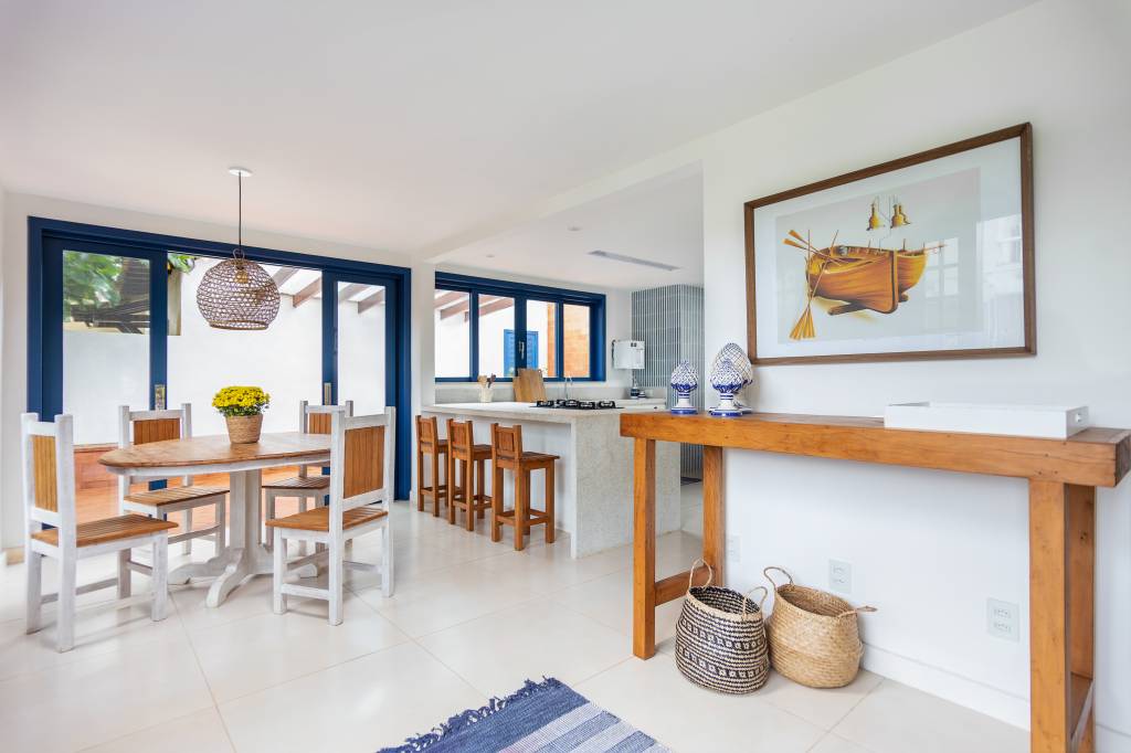 Janelas azuis dão charme a casa de praia em Búzios com suíte térrea escondida por lambris. Projeto de Fernanda Zeitoune. Na foto, sala integrada com cozinha, aparador de madeira.