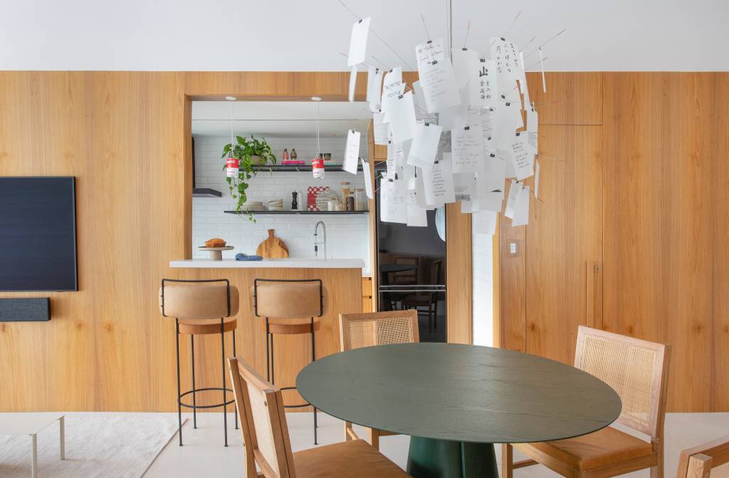 Painel de madeira abraça área social e emoldura cozinha em apê de 90 m²