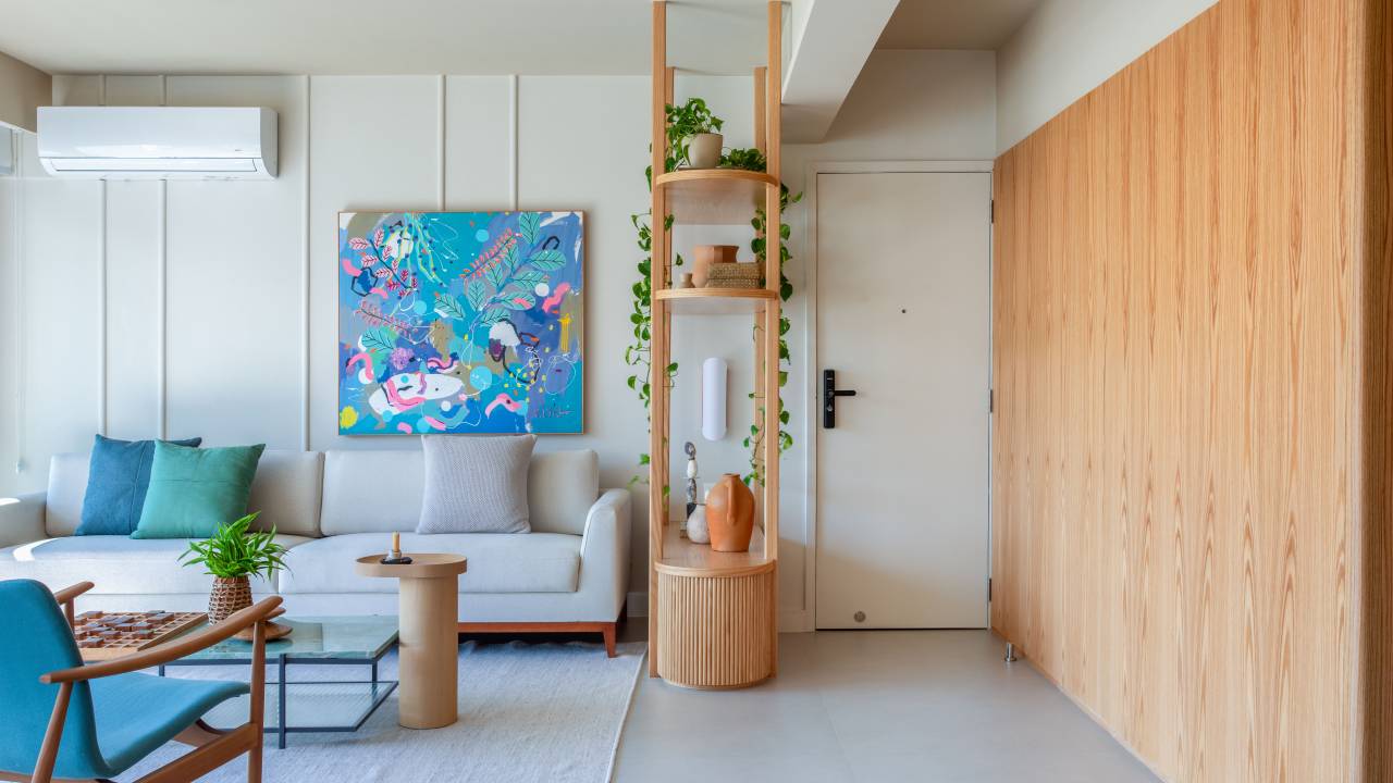Reforma cria quarto de casal com papel de parede degradê e marcenaria multifuncional. Projeto de MBV Arquitetura. Na foto, sala de estar, quadro, estante vazada arredondada, sofá cinza claro.
