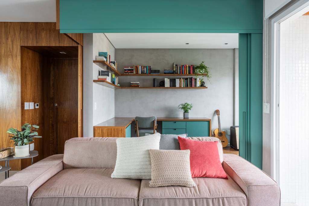 Reforma transforma quarto em home office e o integra a sala com porta de correr verde. Projeto de Adriana Favaro Arquitetura. Na foto, sala de estar, sofá rosa claro queimado, tapete azul, poltronas brancas.