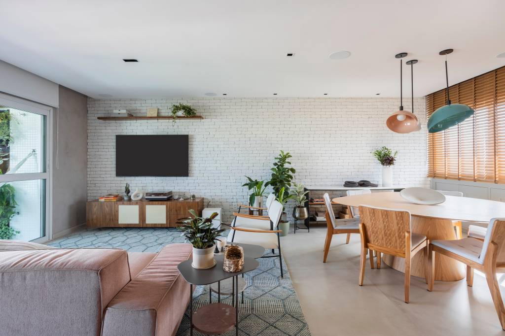 Reforma transforma quarto em home office e o integra a sala com porta de correr verde. Projeto de Adriana Favaro Arquitetura. Na foto, sala integrada, sofá rosa, parede de tjiolinhos brancos, luminária.