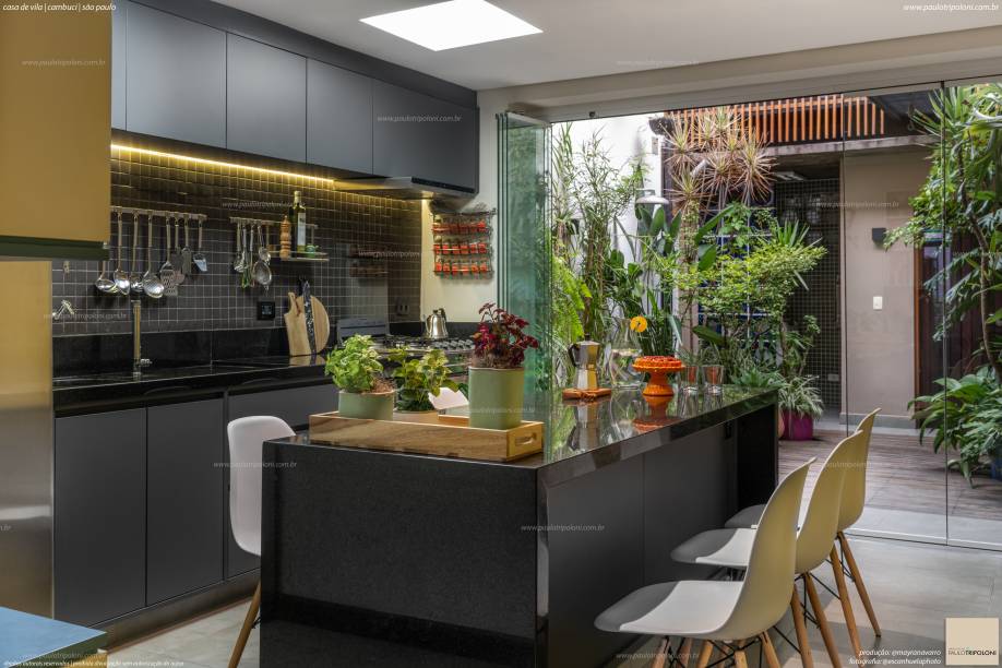 Em um contraponto com a sala de estar, o predomínio do preto e grafite, presente na marcenaria e revestimentos, reflete o estilo atual da cozinha que tem a bancada multifuncional que atua como área complementar para o preparo dos alimentos e mesa. Além da sua finalidade, no projeto realizado pelo arquiteto Paulo Tripoloni, ela foi incumbida de ser a conexão com a área externa. Em um contraponto com a sala de estar, o predomínio do preto e grafite, presente na marcenaria e revestimentos, reflete o estilo atual da cozinha que tem a bancada multifuncional que atua como área complementar para o preparo dos alimentos e mesa. Além da sua finalidade, no projeto realizado pelo arquiteto Paulo Tripoloni, ela foi incumbida de ser a conexão com a área externa.