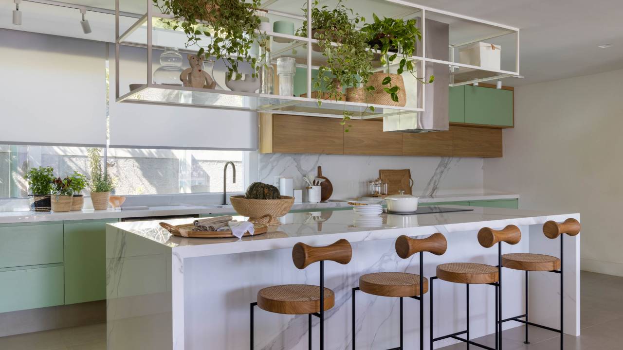 Cobertura ganha cozinha aberta para a sala, hidromassagem e sauna com reforma. Projeto de Paula Neder. Na foto, cozinha integrada, bancada marmorizada, armário verde, banquetas.