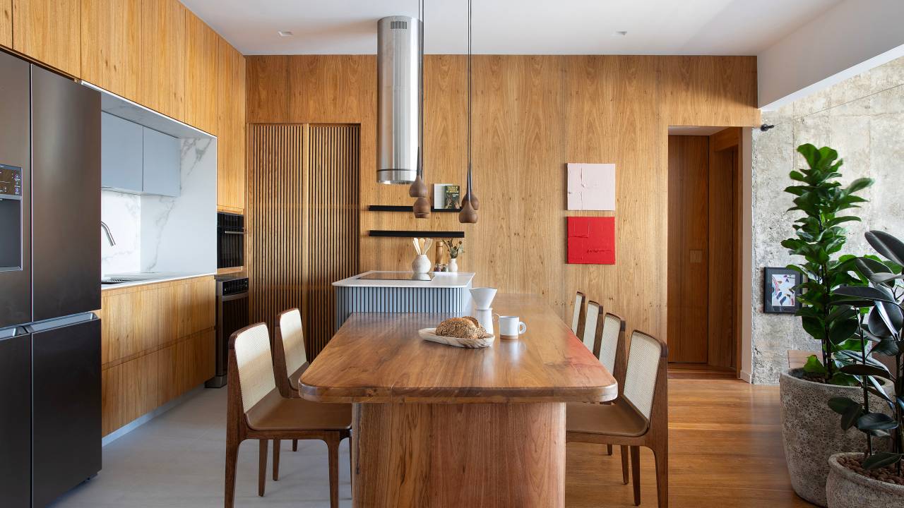 Cozinha vira suíte e sala de jantar vira nova cozinha neste apartamento de 98 m². Projeto de Rafael Ramos. Na foto, cozinha integrada, revestimento de madeira, ilha com bancada.