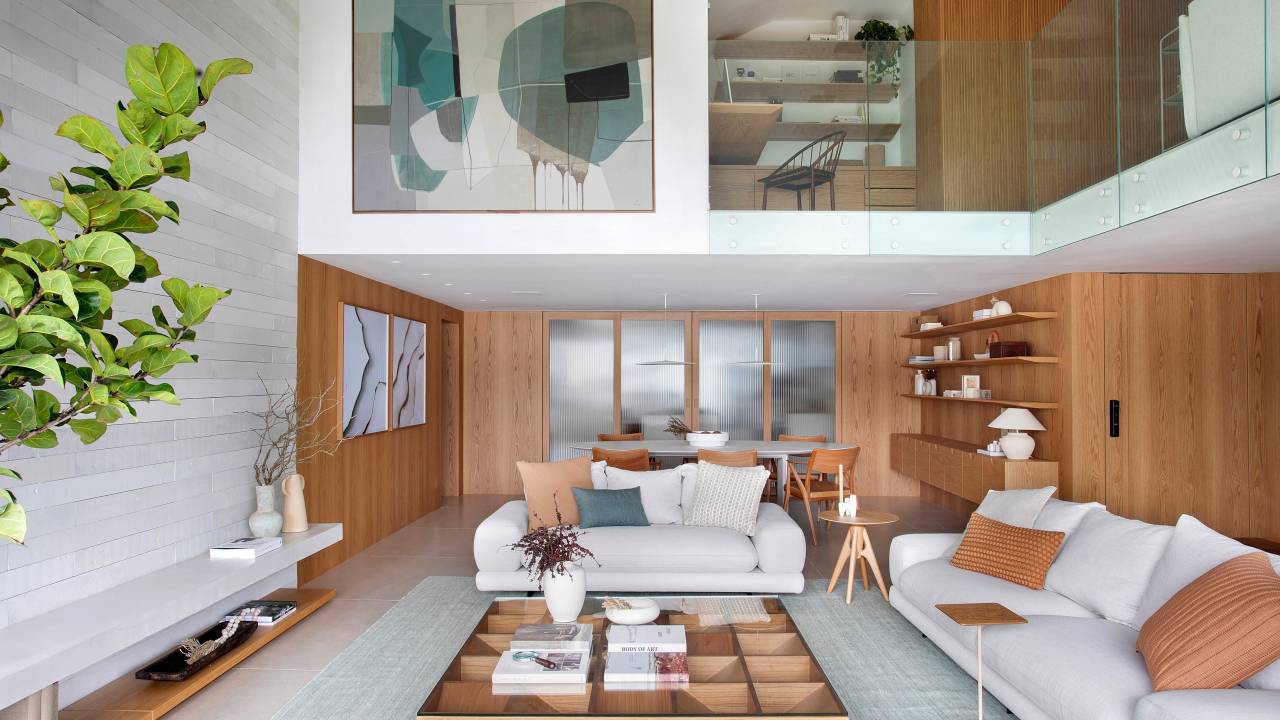 Escada de serralheria branca leva a mezanino com sala de TV e home office em apê. Projeto de Natália Lemos. Na foto, sala de estar, sofá branco.