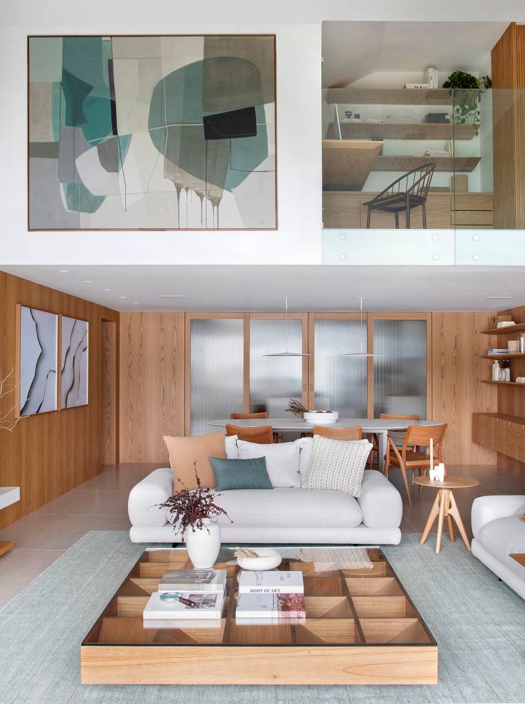 Escada de serralheria branca leva a mezanino com sala de TV e home office em apê. Projeto de Natália Lemos. Na foto, sala de estar, sofá branco.