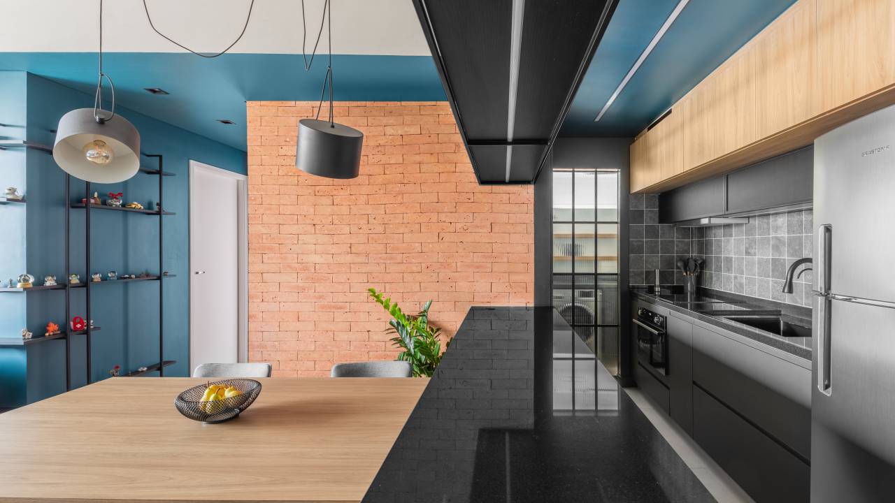 Industrial e leve: apartamento combina serralheria com cores claras e escuras. Projeto de Studio Elã. Na foto, cozinha integrada, bancada preta, parede de tijolinhos.