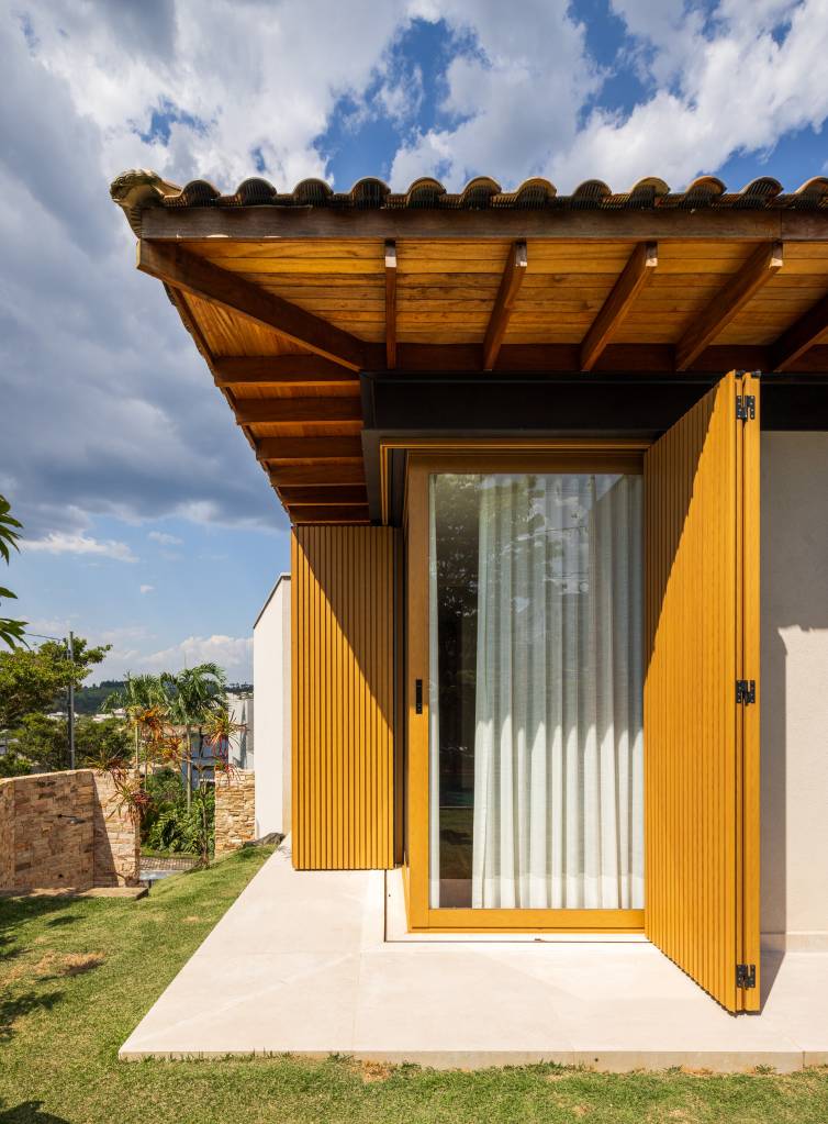 Projeto de casa supera o declive de 5 m do terreno e cria decoração rústica. Projeto de Sabella Arquitetura. Na foto, sala de estar integrada com cozinha com marcenaria verde.