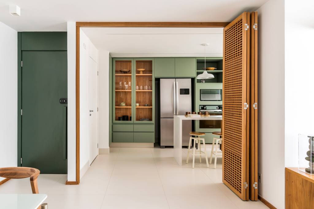 Porta camarão em muxarabi revela cozinha com marcenaria verde em apartamento