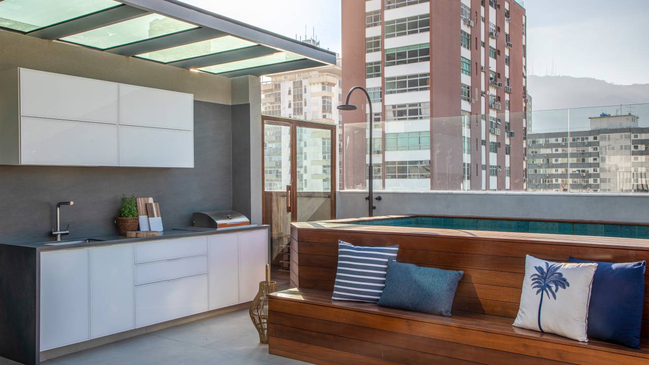 Área de lazer de cobertura ganha cozinha aberta, piscina e banco no deck. Projeto de Roberta Nicolau. Na foto, área externa.