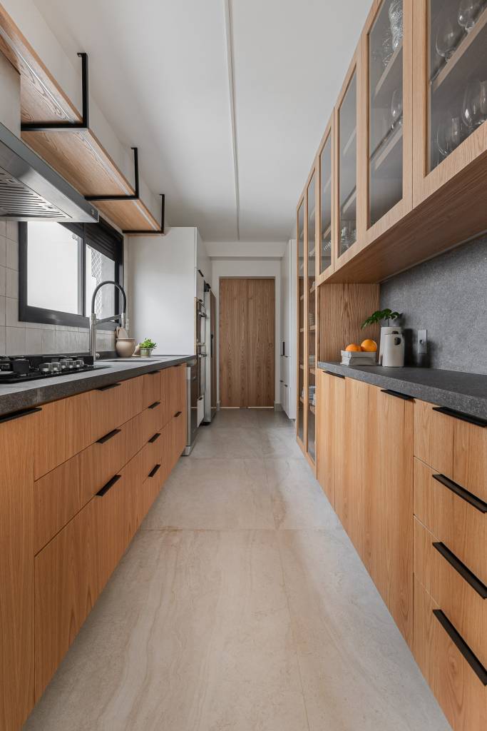 Apartamento de 175 m² se destaca pela parede revestida em pedra moledo. Projeto de Livia Dalmaso Arquitetura. Na foto, cozinha com armários e gavetas.