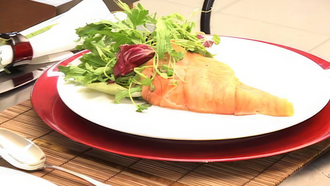 Um elegante buquê de salmão defumado disposto sobre um prato, rodeado por um mix de folhas verdes frescas, como rúcula e agrião. O prato é finalizado com um molho de azeite e limão, conferindo um toque de frescor e sabor ao prato. Ideal para uma apresentação leve e sofisticada em um jantar.